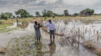 Abuk Deng holds her four year old daughter in her arms as they walk away from their flooded home while an IRC nutrition officer walks alongside them.