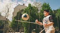 Ein Junge auf Krücken spielt Fußball auf einem sonnigen Spielplatz, konzentriert den Ball mit seinen Krücken jonglierend.